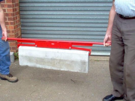 Two people using the red steel end gripping kerb/slab lifter from Mustang to lift a concrete slab