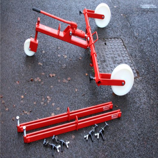 Red steel Mustang hydraulic manhole cover lifter over manhole cover next to 700mm Mustang spreader bars, on concrete