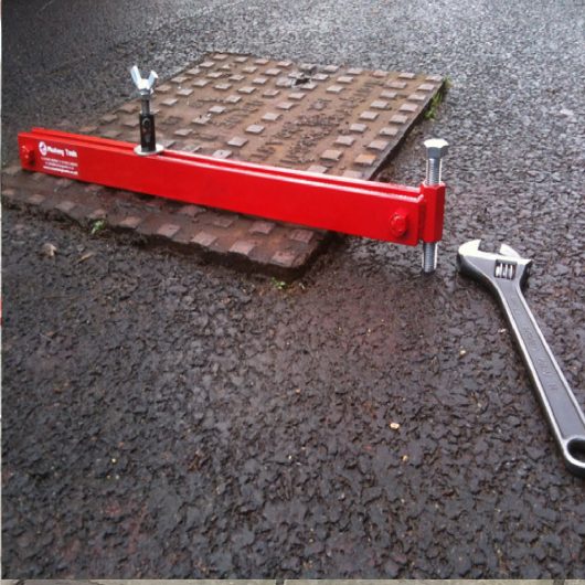 700mm long red steel Mustang manhole cover seal breaker attached to a manhole cover with spanner laying next to it