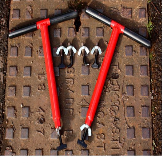 Red steel Mustang mini lift manhole cover lifters with interchangeable keys, laid on a manhole cover