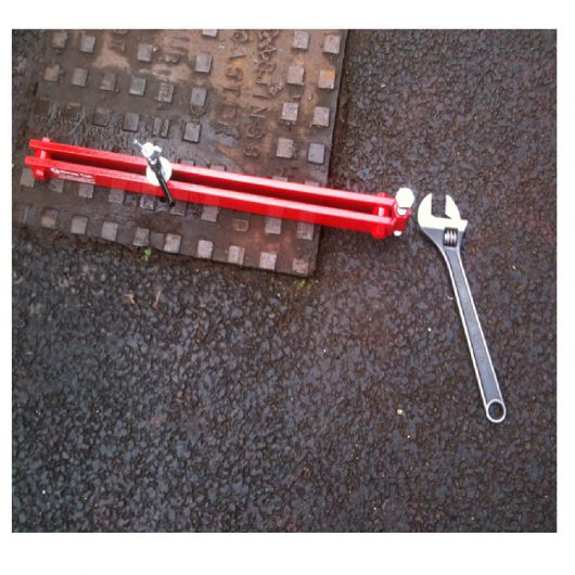 Top view of 700mm long red steel Mustang manhole cover seal breaker attached to a manhole cover with spanner laying next to it