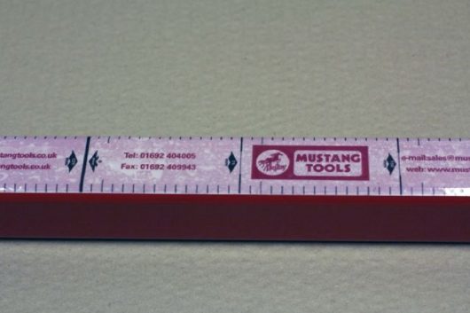 Close up of a strip of gauge tape with black measurement marks, Mustang tools branding and contact details printed on it