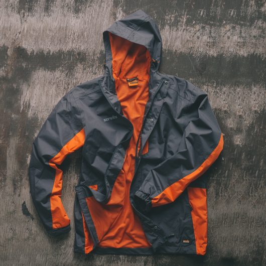 Graphite and orange polyester ripstop Scruffs worker jacket with orange mesh lining laid on a wooden surface