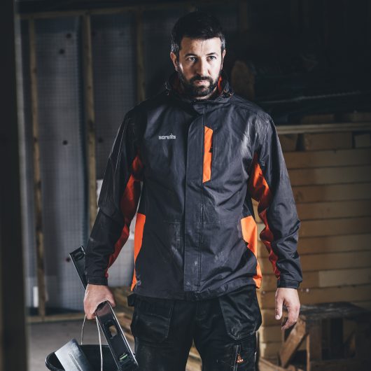 Man holding a spirit level and bucket wearing the orange and graphite Scruffs worker jacket and Scruffs 3d trade trousers